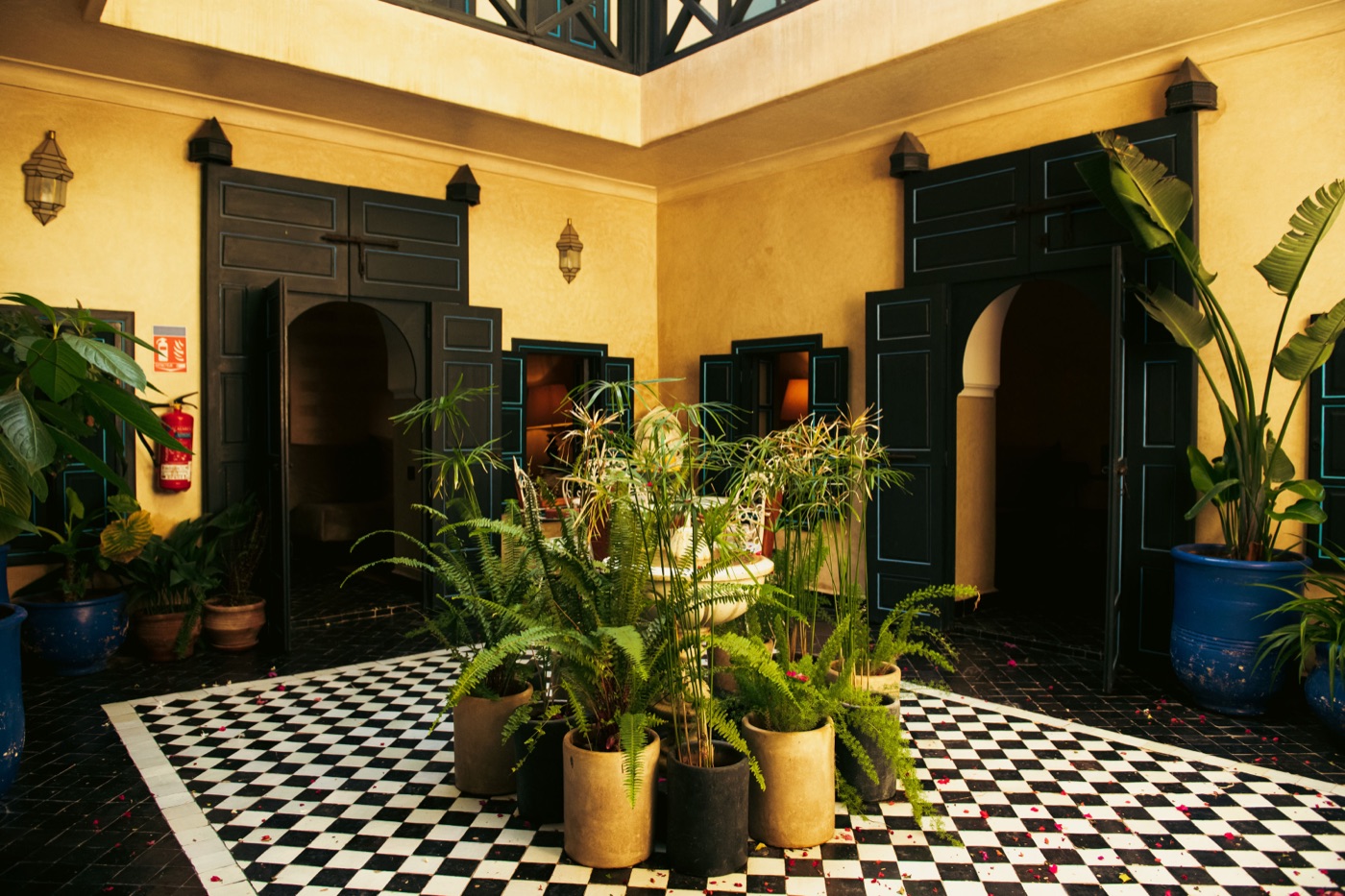 The classic riad&rsquo;s fountain patio in daylight — checkerboard tiles, ochre walls and black shuttered doors