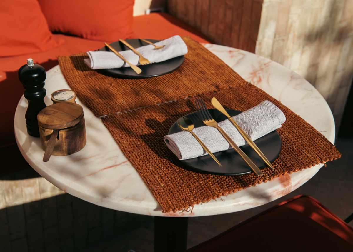 Marble café table laid with brass cutlery and woven raffia mats