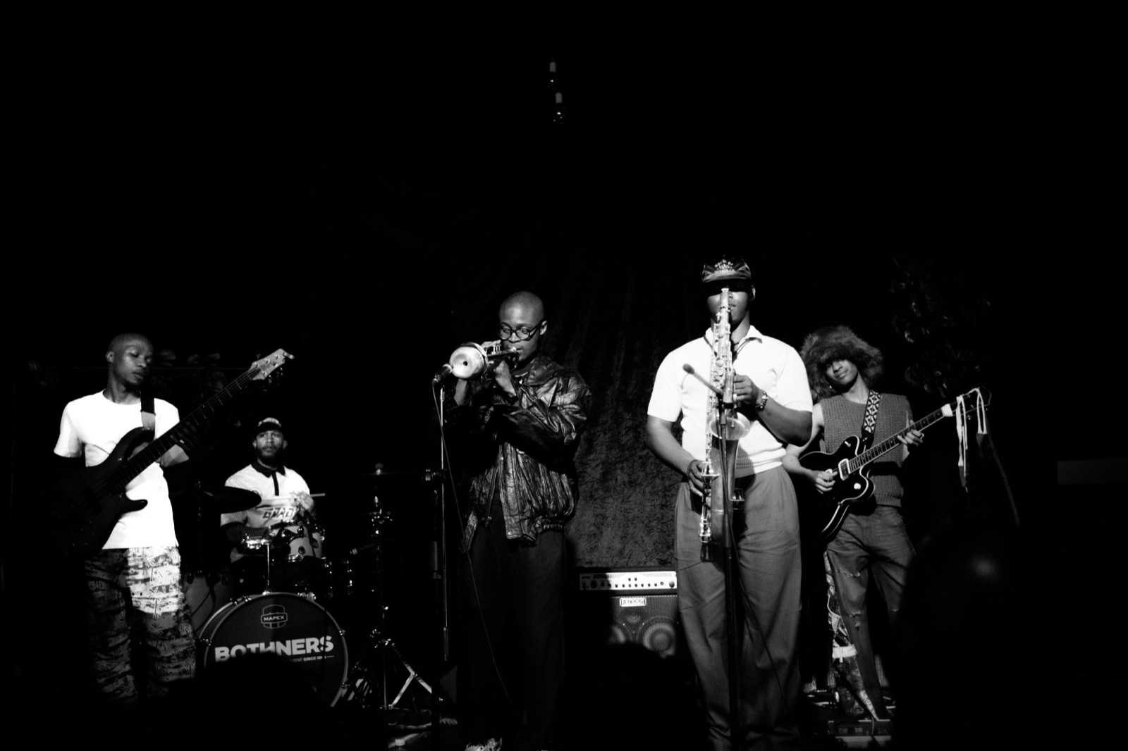 The full band on stage — bass, drums, trumpet, saxophone and guitar